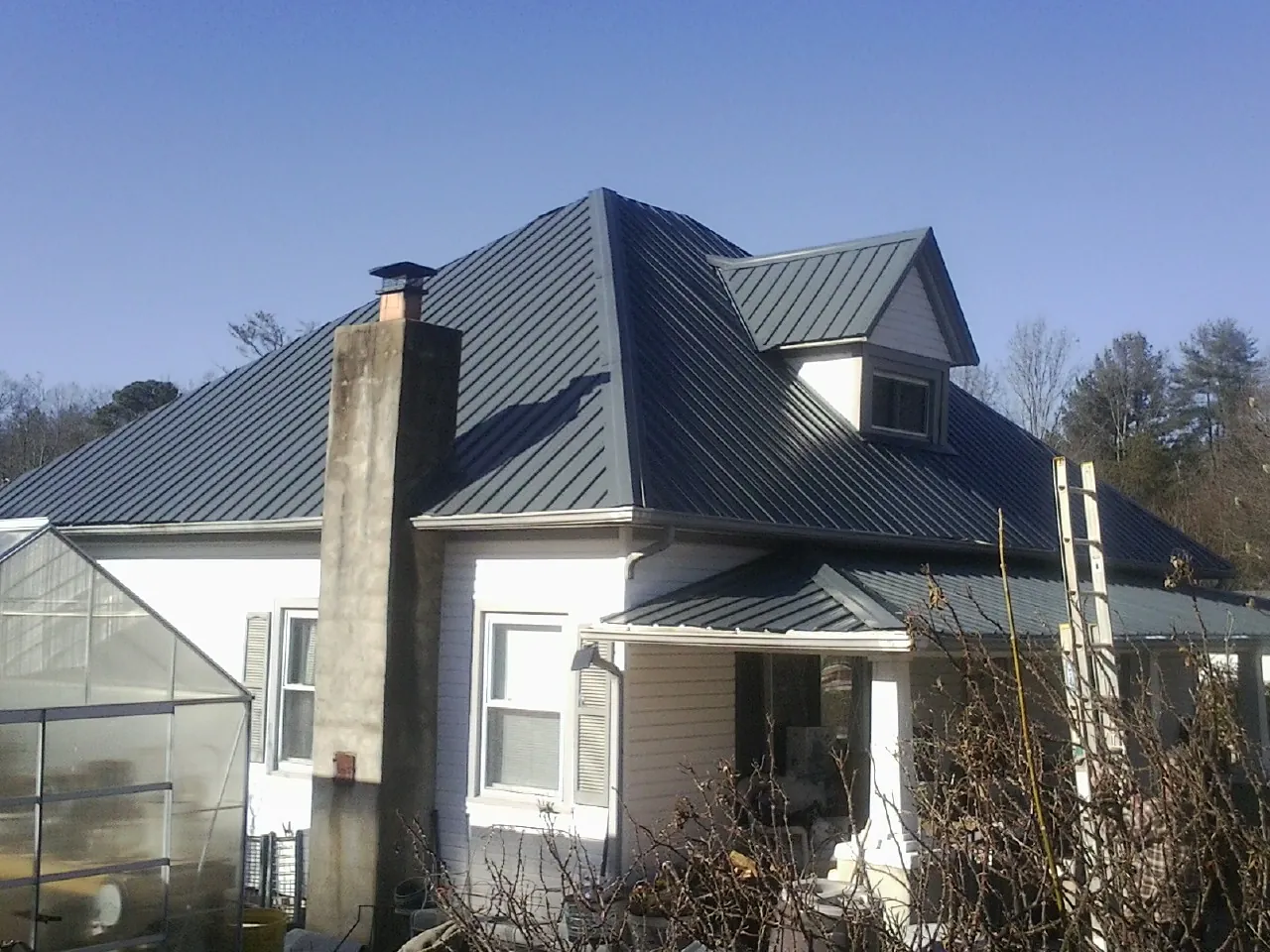 Dark blue standing seam metal roof on a white farmhouse with dormer — Slate & Tile Roof Repair by Roofing Brothers in Nada