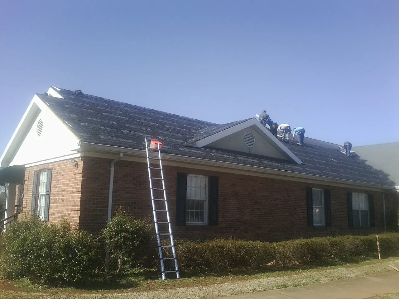 Crew tearing shingles off a brick ranch roof with a ladder set — Emergency Roof Repair work by our crew in Nada