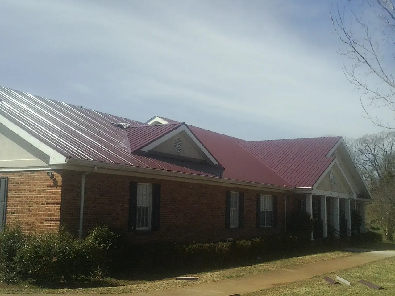 Red metal roof with gabled entries on a long brick building, from a Hail Damage Roof Repair job in Nada