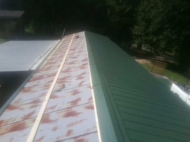 Old rusted panels beside newly installed green metal roofing — Wind Damage Roof Repair by Roofing Brothers in Nada